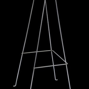 May include: A tall, silver metal easel with a minimalist design. The easel features a three-legged base and a top section with two curved hooks for holding a canvas or artwork. The structure is made of thin, straight metal rods.
