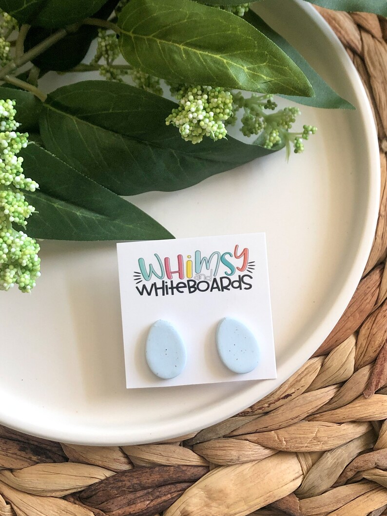 May include: A pair of light blue oval-shaped earrings with a speckled texture. The earrings are on a white card with the text "Whimsy Whiteboards" printed on it.