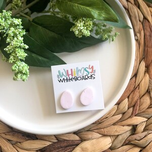 May include: A pair of pink oval-shaped earrings with a speckled texture. The earrings are displayed on a white card with the text "Whimsy Whiteboards".