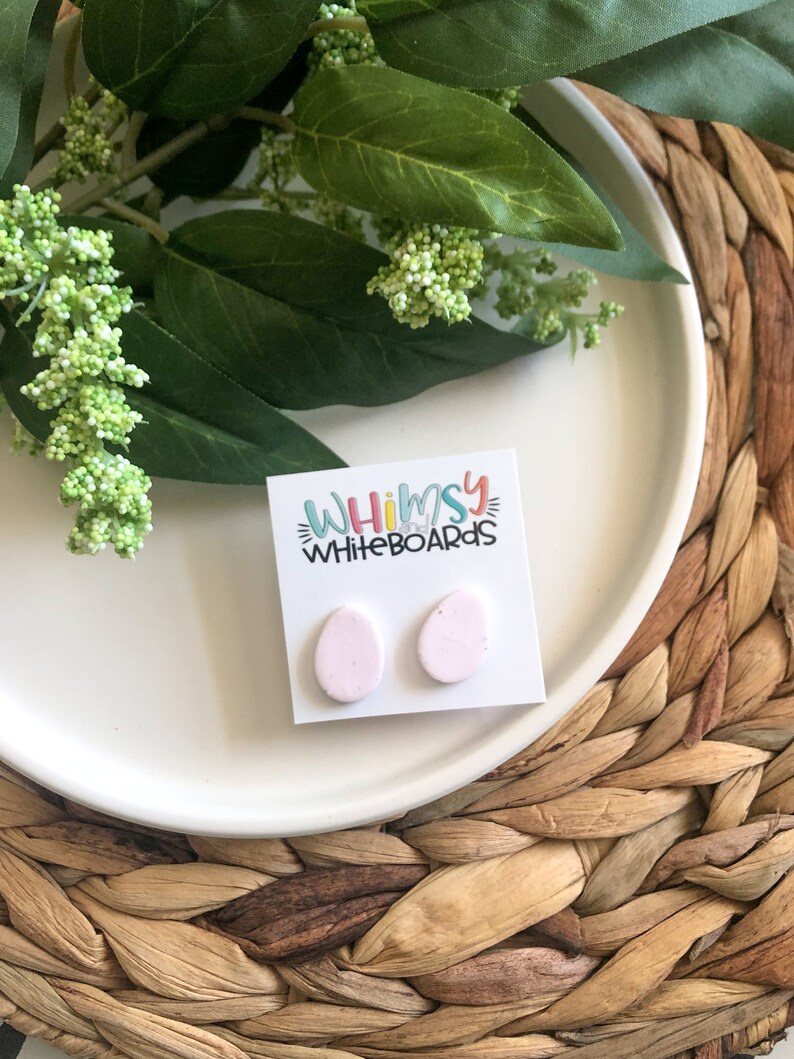 May include: A pair of pink oval-shaped earrings with a speckled texture. The earrings are displayed on a white card with the text "Whimsy Whiteboards".