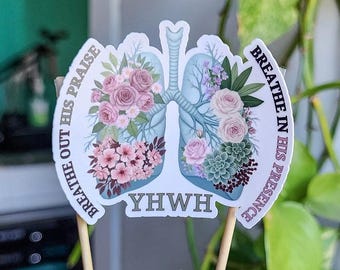 May include: A sticker featuring a stylized illustration of lungs filled with pink and purple flowers and succulents. The text "BREATHE OUT HIS PRAISE" and "BREATHE IN HIS PRESENCE" curves around the edges. The word "YWHW" is at the bottom.