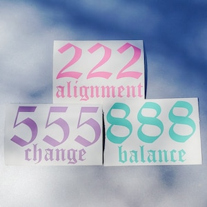 Puede incluir: Tres pegatinas blancas con números y texto rosa, morado y turquesa. La pegatina superior dice "222 alineación". La pegatina del medio dice "555 cambio". La pegatina inferior dice "888 equilibrio".