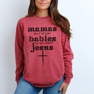 May include: A long-sleeved, red-toned sweatshirt with the text "mamas don't let your babies grow up without jesus" in black lettering. A simple cross is below the text. The sweatshirt is a casual style.