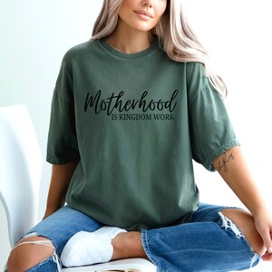 May include: A green t-shirt with the text "Motherhood is Kingdom Work" in black lettering.