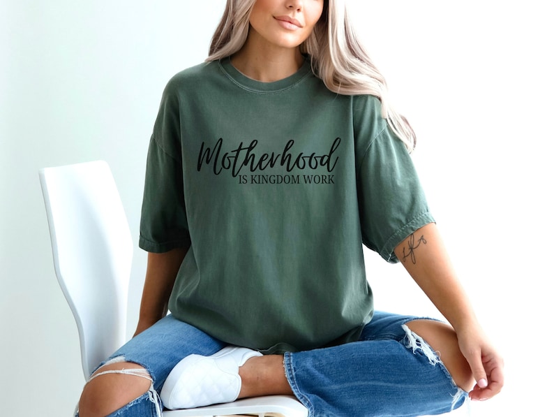 May include: A green t-shirt with the text "Motherhood is Kingdom Work" in black lettering.
