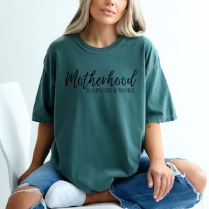 May include: A teal blue t-shirt with the text "Motherhood is Kingdom Work" in black script.