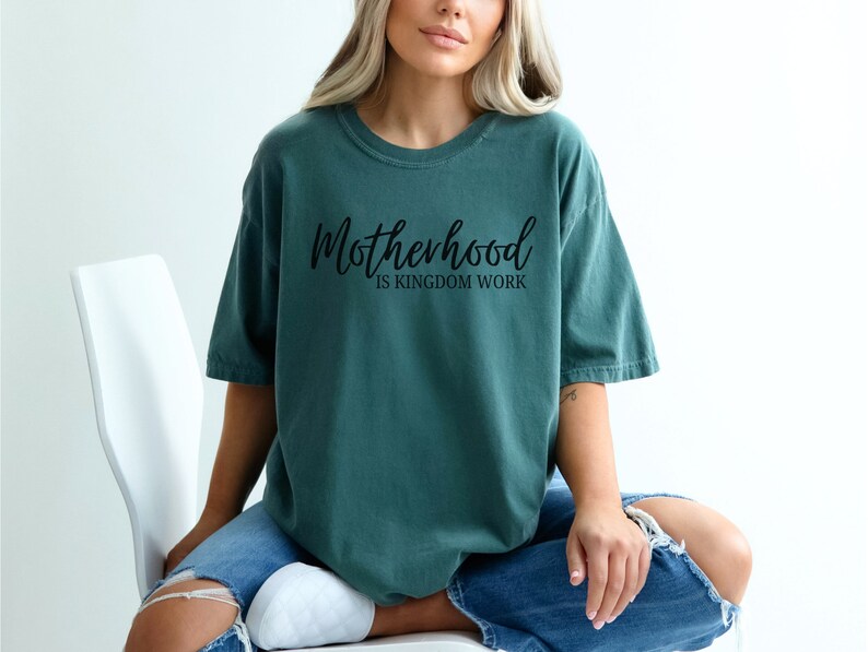 May include: A teal blue t-shirt with the text "Motherhood is Kingdom Work" in black script.