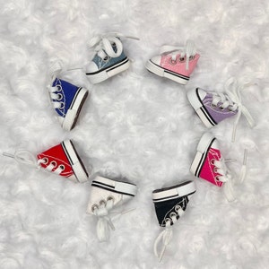 May include: Seven pairs of miniature canvas sneakers in various colors, including red, pink, blue, purple, and black. Each shoe has white laces and a white sole.