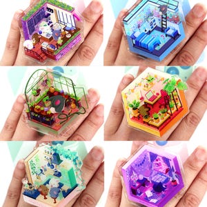 May include: Six hexagonal acrylic charms, each depicting a miniature room scene. The designs include a bedroom, greenhouse, and cafe, with detailed illustrations and vibrant colours. The charms are held in a hand, showcasing the intricate designs.