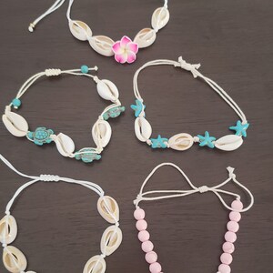 May include: Five different shell bracelets with white string and various charms. The charms include a pink flower, a blue turtle, a blue starfish, and a white starfish.