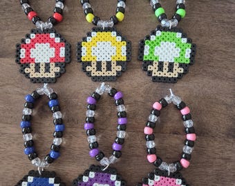 May include: Six colorful mushroom-shaped beaded necklaces. Each necklace features a different color mushroom pendant: red, yellow, green, blue, purple, and pink. The beads on the necklaces are black, clear, and the same color as the mushroom.