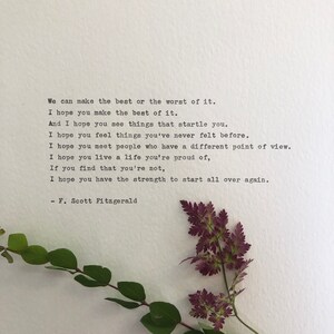 May include: A white paper with a typed quote by F. Scott Fitzgerald and a sprig of greenery. The quote begins, "We can make the best or the worst of it." The greenery includes green leaves and purple flowers.