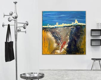 May include: Abstract cityscape painting with a blue sky, a white skyline, and a textured, colorful foreground. The artwork is framed and hangs on a white wall. A silver coat rack and a black tote bag are in the foreground.