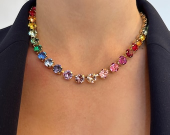 Può includere: Una collana dorata con una serie di pietre preziose colorate. La collana presenta un arcobaleno di colori, tra cui rosso, arancione, giallo, verde, blu e viola. Le pietre preziose sono distanziate uniformemente e incastonate in una catena d'oro.