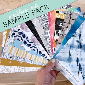 Pode incluir: Um pacote de amostra de papel de parede com uma variedade de padrões e texturas, incluindo mármore aquarela, geométrico e desenhos florais. O pacote inclui o texto "mystery mix SAMPLE PACK" e "Watercolor Marble Texture".