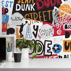 a white desk with a laptop, a cup, and a potted plant. The background behind the desk is covered in a colorful, graffiti-style wall with various words and phrases related to basketball, such as "SLAM", "DUNK", "STREET", "LAW", "WIN", "@", "DUNK", "URBAN", "COOL", "BRO", and "BALLS".