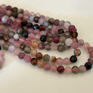 Puede incluir: Una hebra de cuentas de piedras preciosas facetadas en tonos rosa, verde y negro. Las cuentas miden aproximadamente 4 mm y tienen una forma ligeramente irregular.