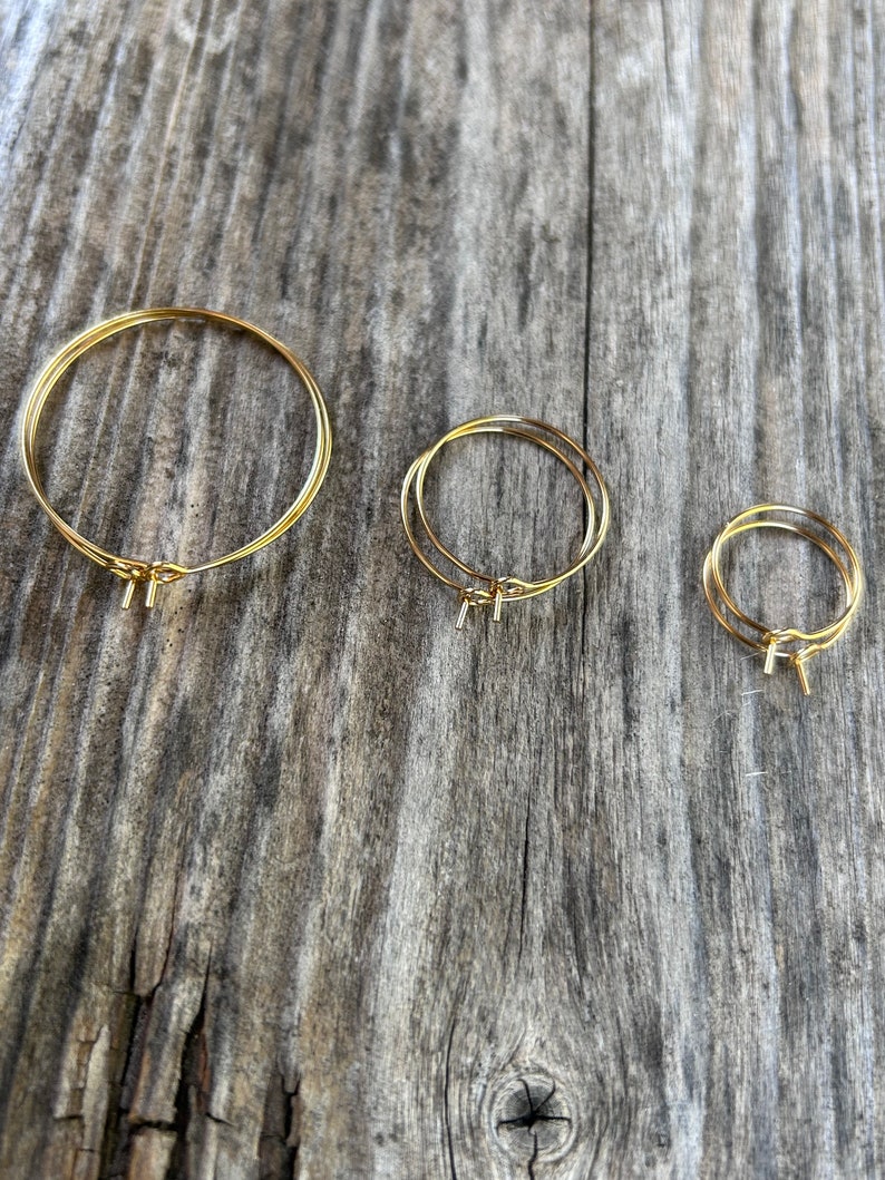 Puede incluir: Tres pendientes de aro dorados de diferentes tama&ntilde;os, mostrados sobre una superficie de madera.