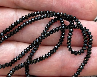 May include: A strand of black faceted beads. The beads are small and round, and they are strung on a clear thread.