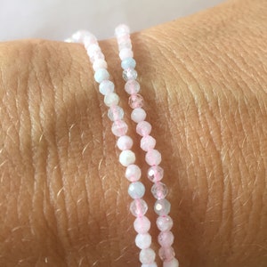 Peut inclure: Deux bracelets délicats faits de petites perles facettées. Un bracelet est bleu clair et l'autre est rose.
