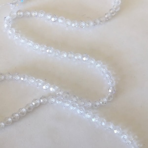Könnte beinhalten: Strang aus klaren, facettierten Kristallperlen. Die kleinen, runden Perlen sind zu einem flexiblen Strang aufgereiht. Die Kristalle reflektieren das Licht und erzeugen einen funkelnden Effekt. Ideal für Schmuckherstellung oder Bastelprojekte.