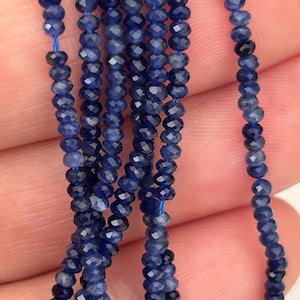 Puede incluir: Hebras de cuentas facetadas de zafiro azul oscuro. Las cuentas están ensartadas en un fino cordón azul, creando una apariencia delicada y elegante. Las piedras preciosas tienen un acabado brillante y pulido, que refleja la luz. Ideal para la fabricación de joyas.