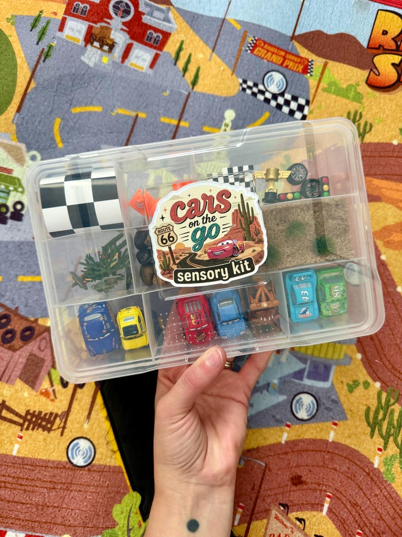 May include: A clear plastic container filled with miniature toy cars and accessories. The container is labeled "Cars on the Go" with a Route 66 theme. Includes a checkered flag, miniature trees, and other racing-themed items.
