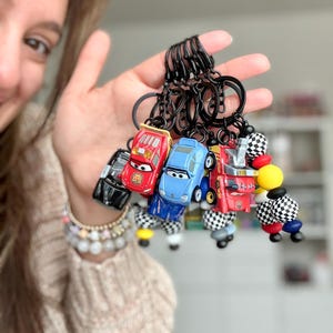 May include: A collection of toy car keychains in various colors, including red, blue, and black. Each keychain features a miniature car design with black key rings. Some keychains have checkered flag accents.