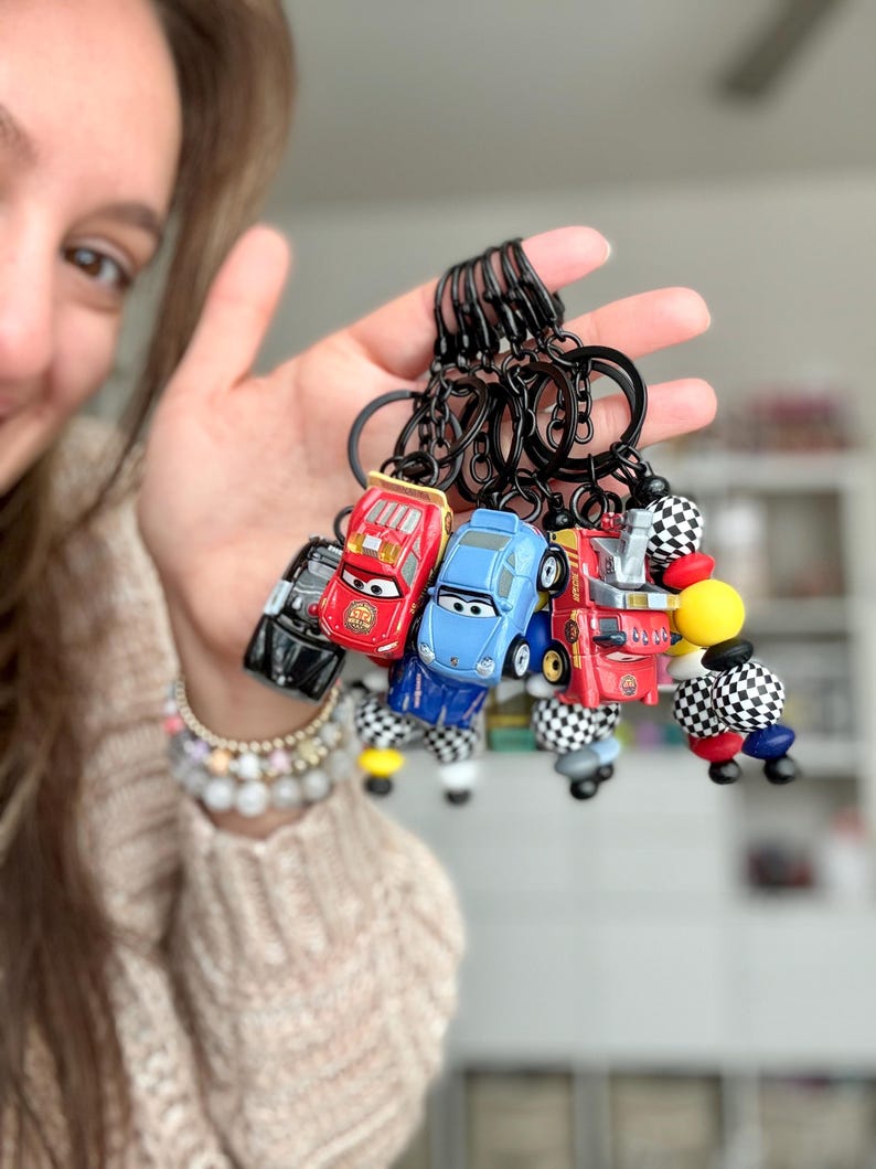 May include: A collection of toy car keychains in various colors, including red, blue, and black. Each keychain features a miniature car design with black key rings. Some keychains have checkered flag accents.