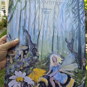 Pode incluir: Um calendário de parede 2027 intitulado ARTelier Doris Artmann com uma ilustração em aguarela de uma cena florestal com uma fada montada num grande abelhão, rodeada por cogumelos, um veado, um esquilo, um escaravelho e flores silvestres.