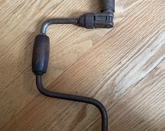 Puede incluir: Un taladro de manivela vintage con un mango de madera y una manivela de metal. El taladro está hecho de metal y tiene un acabado negro. Es una herramienta útil para perforar agujeros en la madera.