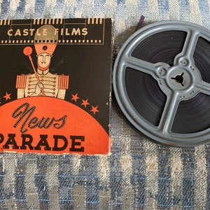 May include: A vintage film reel with a black and white film strip. The reel is labeled "News Parade" and "Castle Films" in red and black lettering. The label also features a cartoon illustration of a drum major in a red and gold uniform.