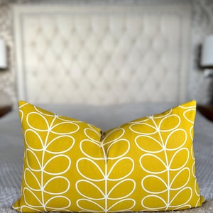 Può includere: Cuscino rettangolare giallo senape con un motivo a foglie bianche. Il cuscino è posto su un letto grigio, con una testiera bianca sullo sfondo. Un accessorio decorativo per la casa.