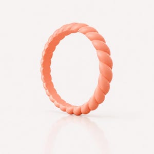 Puede incluir: Un anillo de color melocotón sólido que presenta una textura trenzada continua similar a una cuerda en toda la banda. El anillo tiene un acabado mate y una forma circular uniforme, mostrando un diseño consistente alrededor del aro.