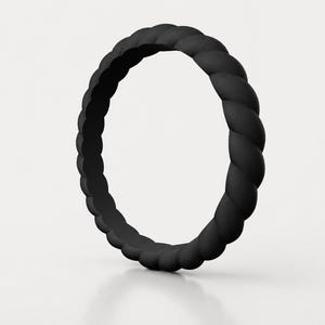 Puede incluir: Un anillo negro mate que presenta un diseño de cuerda trenzada continua. La banda tiene una forma circular uniforme con una superficie texturizada que imita la apariencia de un cordón trenzado, creando un patrón constante alrededor.