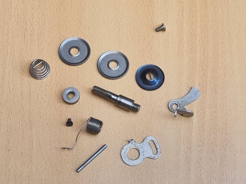 May include: Assortment of silver-toned metal sewing machine parts, including a spring, a small screw, a metal rod, a small metal disc, a metal lever, and a metal gear.