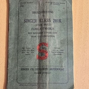 May include: A green instruction manual for a Singer Class 201K sewing machine. The cover features the Singer logo and the text "BRUKSANVISNING FOR SINGER KLASS 201K (UTOM 201K2) FAMILJESYMASKIN MED ROTERANDE GRIPARE SAMT FRAM OCH ATERMATNING".