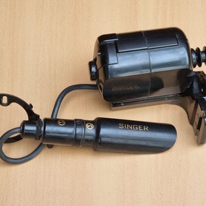 May include: A black Singer sewing machine motor with a black cord and a black foot pedal. The motor has a gold Singer logo on the side. The foot pedal has a gold S on each side.