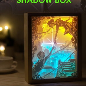 May include: A paper art shadow box with a light blue, yellow, and orange color scheme. The box features a 3D silhouette of two people reaching towards each other. The text "PAPER ART SHADOW BOX" is displayed at the top of the image.