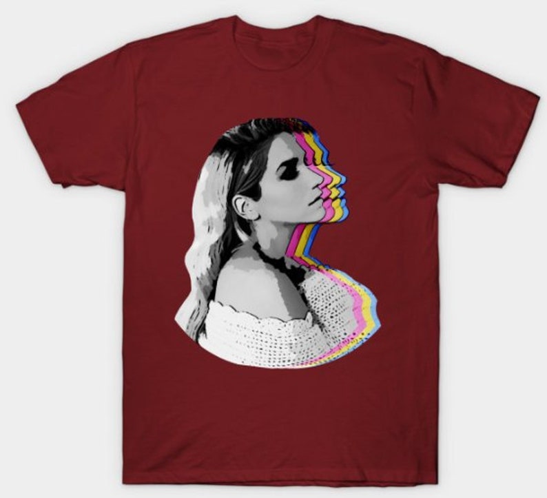 May include: A maroon t-shirt with a graphic of a woman's face with a colorful, layered effect. The woman is looking to the right and has blonde hair.