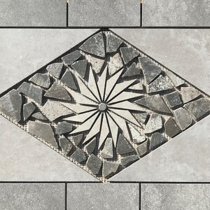 May include: A diamond-shaped mosaic tile with a white starburst design surrounded by gray and black stone pieces.