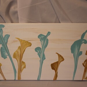 Puede incluir: Pintura abstracta sobre lienzo con formas florales estilizadas en tonos turquesa y dorado sobre fondo blanco.