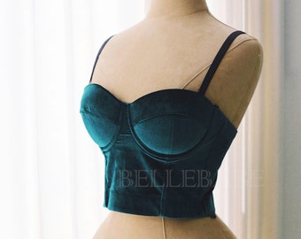 May include: A teal velvet bustier with black straps. The bustier has a boned bodice and a sweetheart neckline.