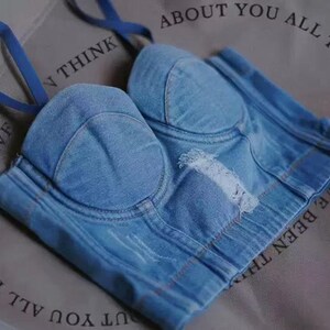 May include: A light blue denim bustier with a sweetheart neckline and adjustable straps. The bustier has a distressed look with frayed edges and a few holes.