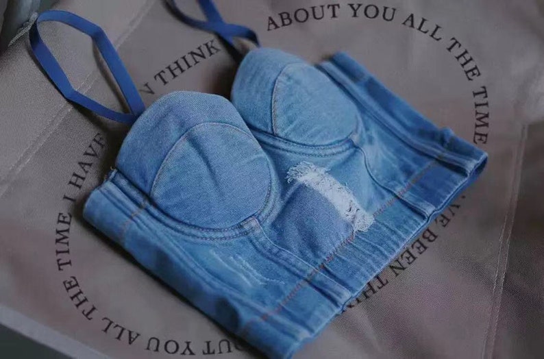 May include: A light blue denim bustier with a sweetheart neckline and adjustable straps. The bustier has a distressed look with frayed edges and a few holes.