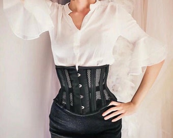Può includere: Un corsetto in rete nera con una camicia bianca abbottonata e una gonna nera.