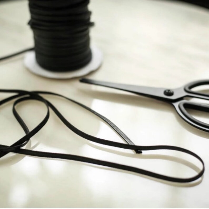 May include: A spool of black leather cord with a length of cord lying next to it and a pair of black scissors.