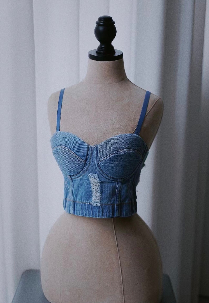 May include: A blue denim corset top with adjustable straps. The top has a sweetheart neckline and is made of a distressed denim fabric.