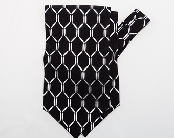 May include: A black necktie with a repeating silver chain-link pattern. The tie is folded and angled, showcasing the geometric design. The tie is made of a smooth fabric and is suitable for formal or business attire.