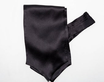 May include: A black satin ascot tie, displayed on a white background. The tie is folded and has a smooth, shiny texture. The ascot is a formal neckwear accessory.
